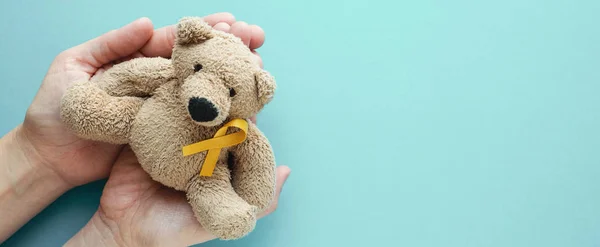 Mãos segurando crianças brinquedo macio urso marrom com fita de ouro amarelo — Fotografia de Stock