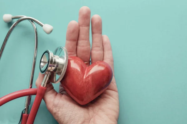 Corazón rojo en la mano con estetoscopio, salud del corazón, seguro de salud — Foto de Stock