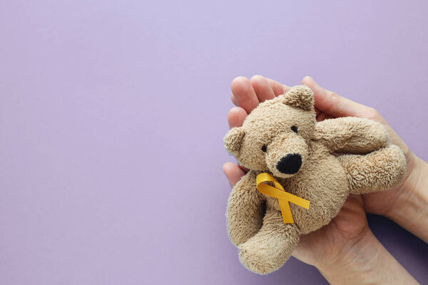 Hands holding children soft toy brown bear with yellow gold ribb