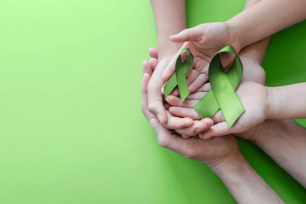 Tangan dewasa dan anak-anak memegang Lime Green Ribbon pada backgro hijau — Stok Foto