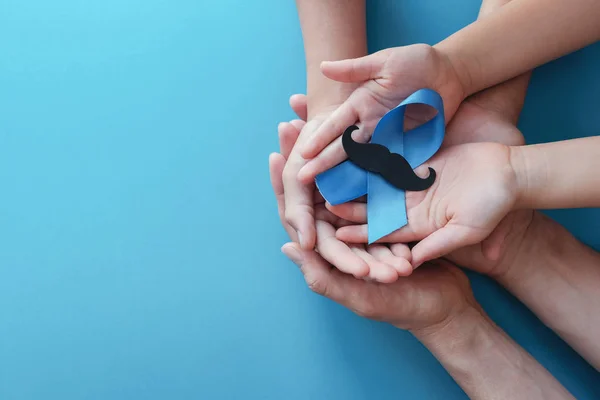 Familiehanden houden licht blauwe ribbonmet snor op blauwe rug — Stockfoto