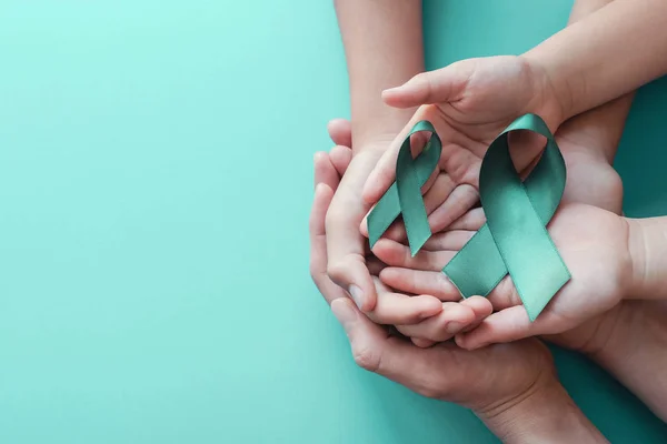 Adulto e crianças mãos segurando fitas Teal no fundo azul — Fotografia de Stock