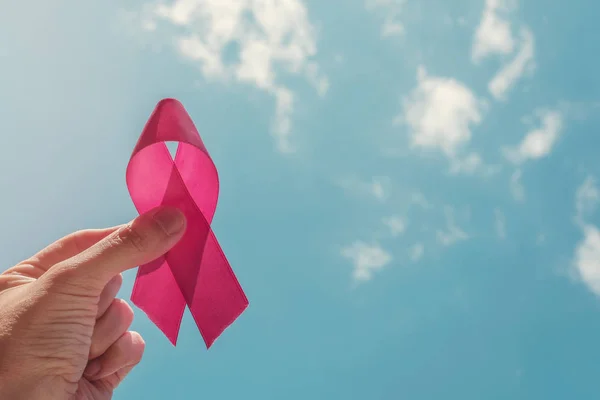 Mão segurando fita rosa no fundo do céu azul, câncer de mama a — Fotografia de Stock