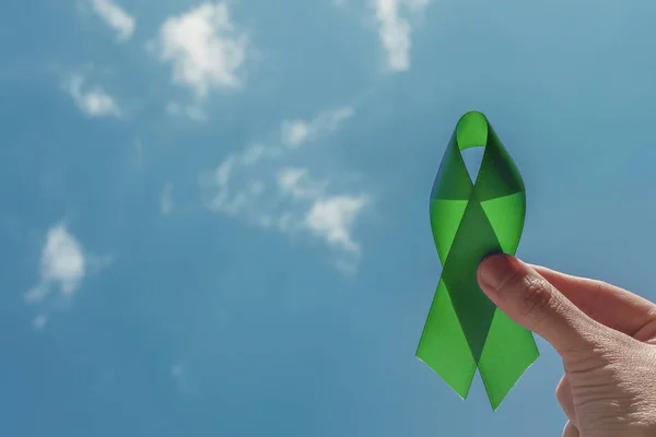 Mão segurando fita verde sobre o céu azul, consciência de saúde mental — Fotografia de Stock
