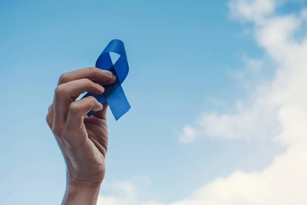 Man Hands holding blue ribbon over blue sky, Prostate Cancer Awa — Stock Photo, Image