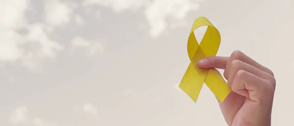 手は灰色の空に黄色の金のリボンを保持 肉腫意識 小児がん意識 9月黄色 世界自殺予防の日の概念 — ストック写真