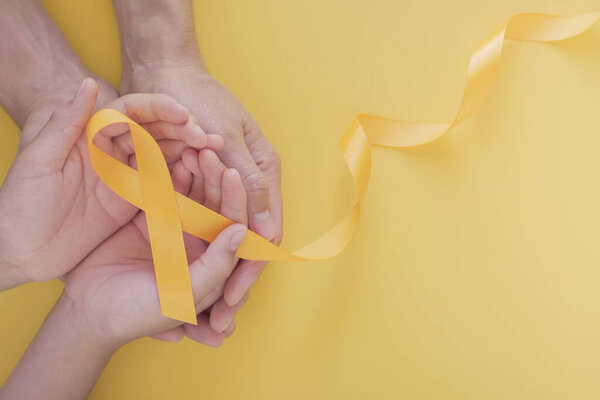 adult and child hands holding yellow gold ribbon, Sarcoma Awareness, Bone cancer, childhood cancer awareness, world suicide prevention day, September Yello