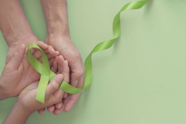 Yetişkin ve çocuk elleri yeşil arka planda Kireç Yeşil Kurdele, çocukların zihinsel sağlık bilinci ve lenfoma farkındalığı, dünya ruh sağlığı günü, dünya böbrek günü
