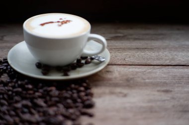 Eski ahşap masa arkasında kahve fincanı ve kahve çekirdekleri. Mesaj için yer var.