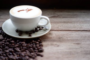 Eski ahşap masa arkasında kahve fincanı ve kahve çekirdekleri. Mesaj için yer var.