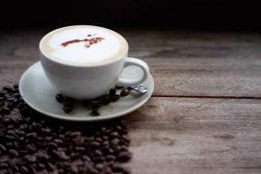 Eski ahşap masa arkasında kahve fincanı ve kahve çekirdekleri. Mesaj için yer var.