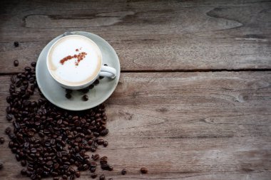 Eski ahşap masa arkasında kahve fincanı ve kahve çekirdekleri. Mesaj için yer var.