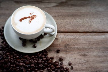 Eski ahşap masa arkasında kahve fincanı ve kahve çekirdekleri. Mesaj için yer var.