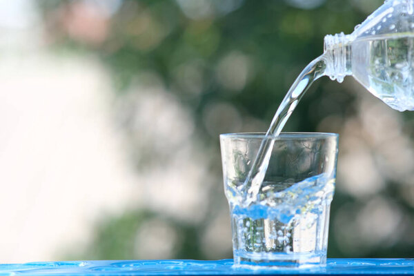 Стакан воды на фоне деревянного стола и наливание питьевой воды
