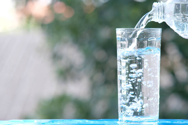 Стакан воды на фоне деревянного стола и наливание питьевой воды
