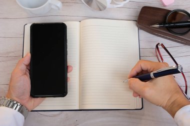 Üst düzey bir iş adamı elinde akıllı bir telefonla masada çalışıyor.