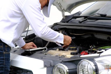 Bozuk bir arabanın üzerinde oturan Asyalı genç adam yardım istiyor.