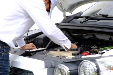 Bozuk bir arabanın üzerinde oturan Asyalı genç adam yardım istiyor.