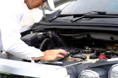 Bozuk bir arabanın üzerinde oturan Asyalı genç adam yardım istiyor.