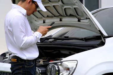 Bozuk bir arabanın üzerinde oturan Asyalı genç adam yardım istiyor.