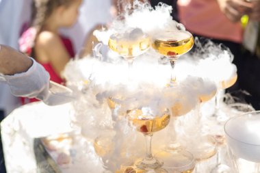 Champagne slide. Pyramid or fountain made of champagne glasses with cherry and steam from dry ice clipart