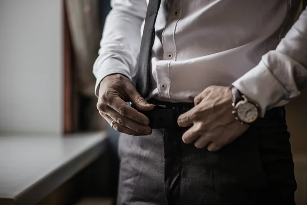 Groom in black tuxedo and bowtie correct his buttons on white shirt. Wedding. Details