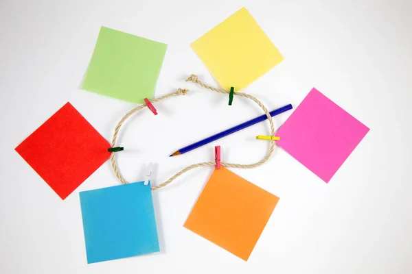 Post-it notes with small colored pegs in a rope and ablue pencil in white background