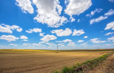 Yüksek gerilim dikmesi bulutlu bir mavi gökyüzü altında ekilmemiş alanlarla