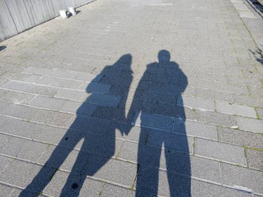 Bir çift, erkek ve kadın sokakta el ele tutuşarak gölgeler.