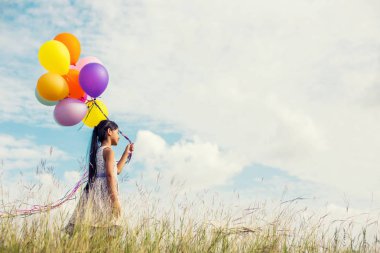 Eller yayılan renkli balonlar çayırda holding mavi gökyüzü ve bulutlar, karşı sevimli küçük kız.