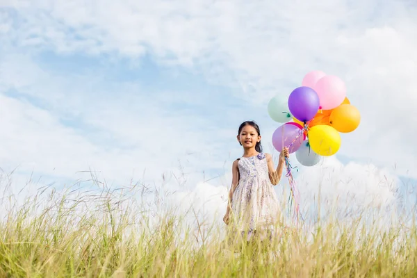 かわいい女の子に対して青い空と雲 牧草地にカラフルな風船を保持手を広める — ストック写真