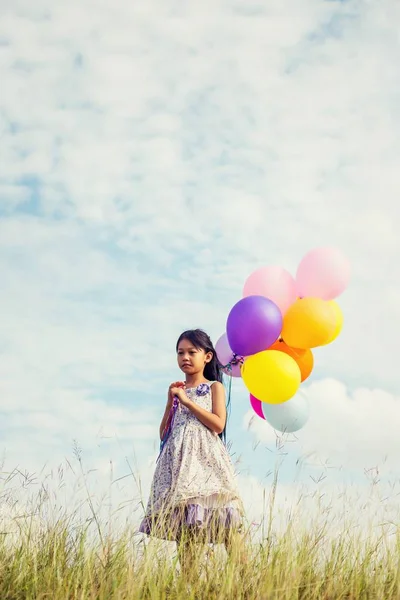 可爱的小女孩拿着五颜六色的气球在草地上对蓝天和云彩 传播的手 — 图库照片