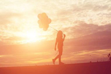 renkli balon gün batımı ile tutan genç kadın silüeti