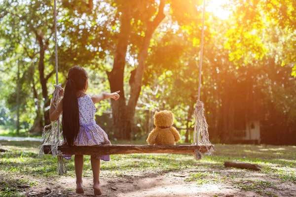 ブランコに座っている小さな女の子とテディベア — ストック写真