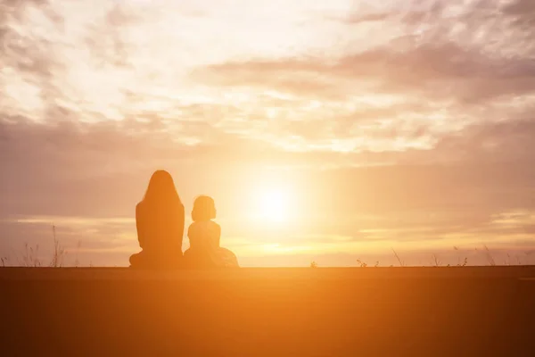 一个快乐的小女孩的剪影 他亲爱的母亲的双臂拥抱 在一个夏日的天空中的日落面前 — 图库照片
