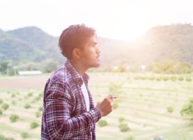 Hipster adam duman sigara, bir dağın duruyor. Sabah temiz havada arasında.