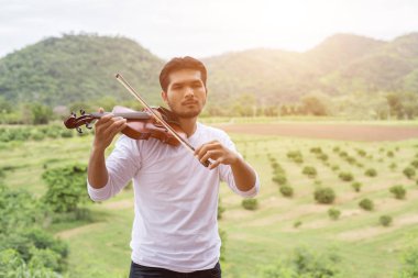 Genç yenilikçi müzisyen adam dağın arkasında doğa açık hava yaşam tarzı içinde keman çalıyor.
