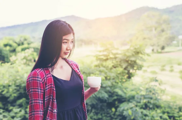Sabah, arkasında dağ manzaralı bir fincan kahve tutan güzel kadın portresi.
