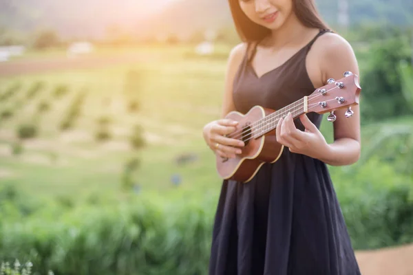 Beautiful woman holding a guitar on his shoulder, Nature park summer outside.