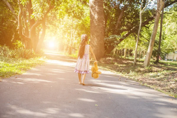 Küçük tatlı kız salıncakta sallanıyor, oyuncak ayı yanında oturuyor, küçük kız ağacı işaret ediyor..