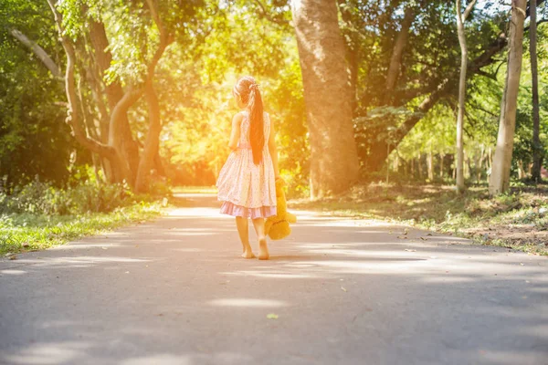 Küçük tatlı kız salıncakta sallanıyor, oyuncak ayı yanında oturuyor, küçük kız ağacı işaret ediyor..