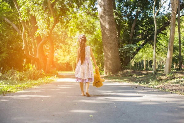 Küçük tatlı kız salıncakta sallanıyor, oyuncak ayı yanında oturuyor, küçük kız ağacı işaret ediyor..