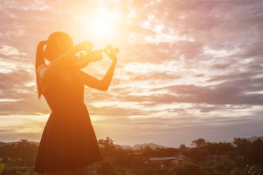 Genç kadın arka planda dağlar ile keman çalıyor