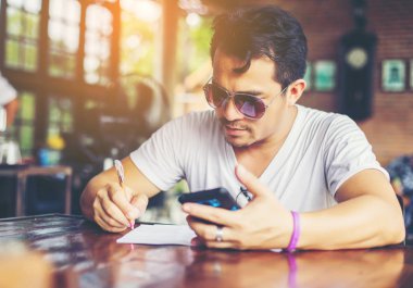 Café'de rahatlatıcı gülümseyen smartphone ile genç adam.