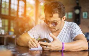 Café'de rahatlatıcı gülümseyen smartphone ile genç adam.