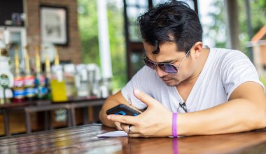 Café'de rahatlatıcı gülümseyen smartphone ile genç adam.