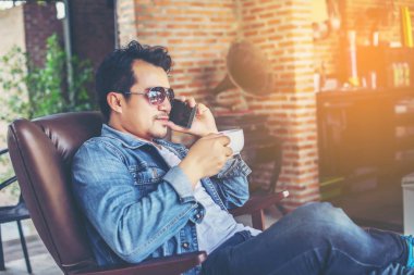 Café'de rahatlatıcı gülümseyen smartphone ile genç adam.