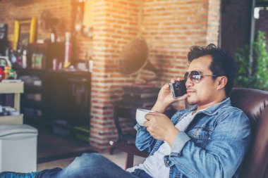 Café'de rahatlatıcı gülümseyen smartphone ile genç adam.