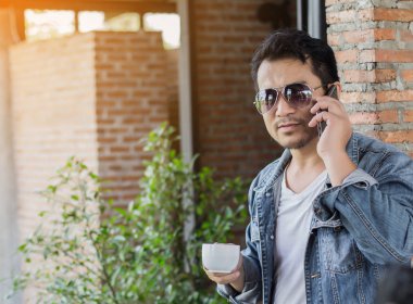 Café'de rahatlatıcı gülümseyen smartphone ile genç adam.