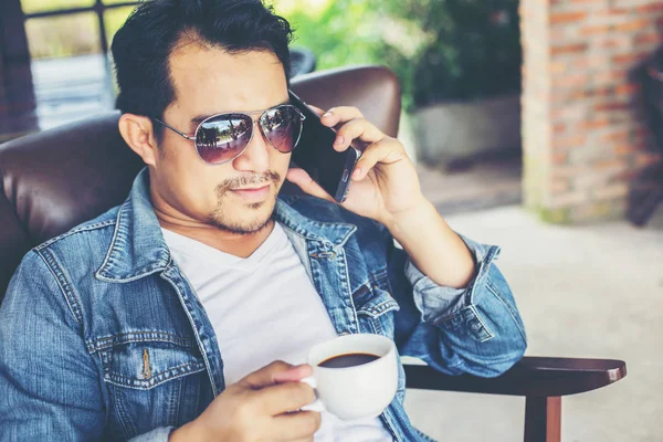 Café'de rahatlatıcı gülümseyen smartphone ile genç adam.